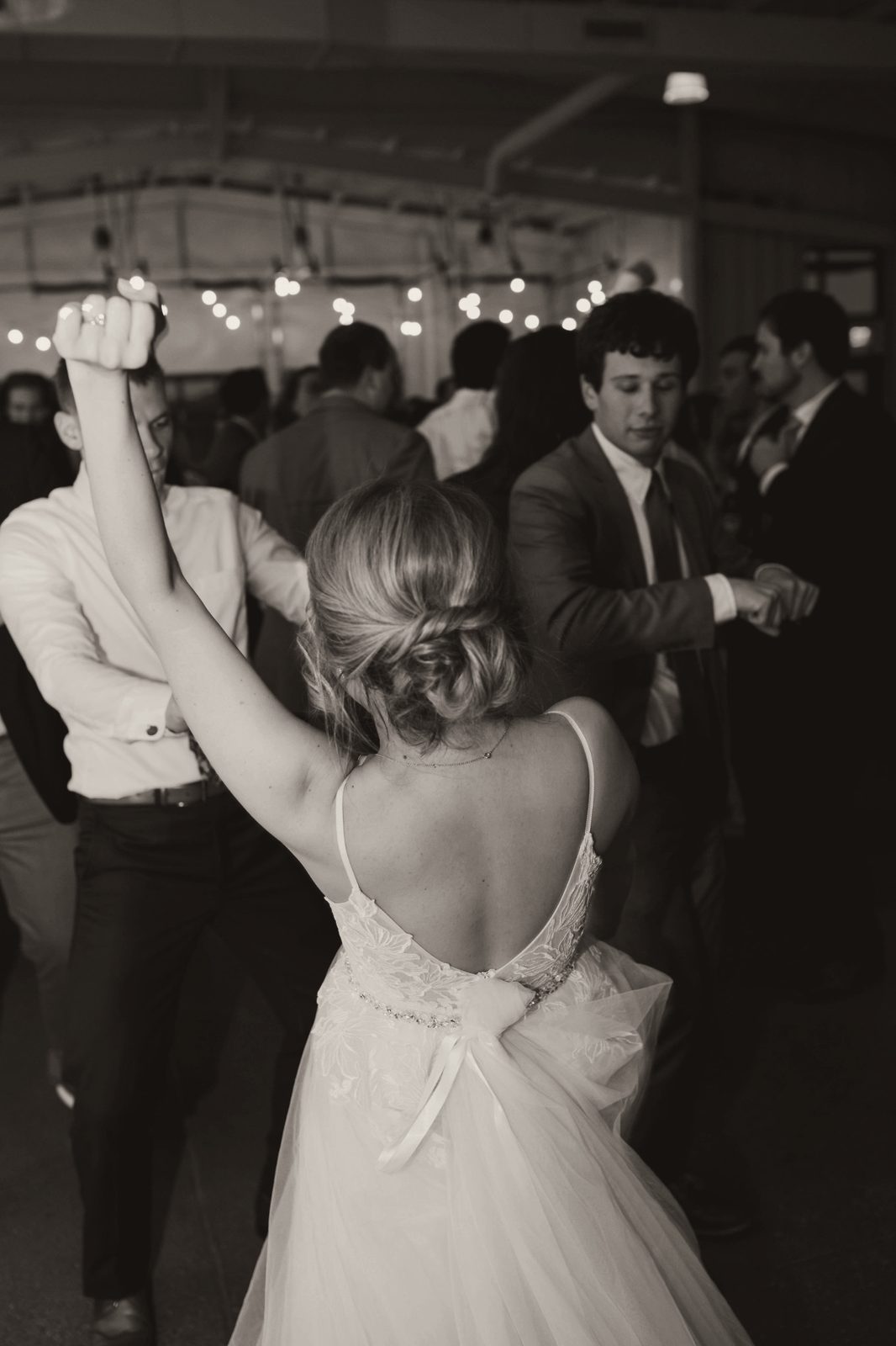 A bride dancing with her arm raised, surrounded by friends