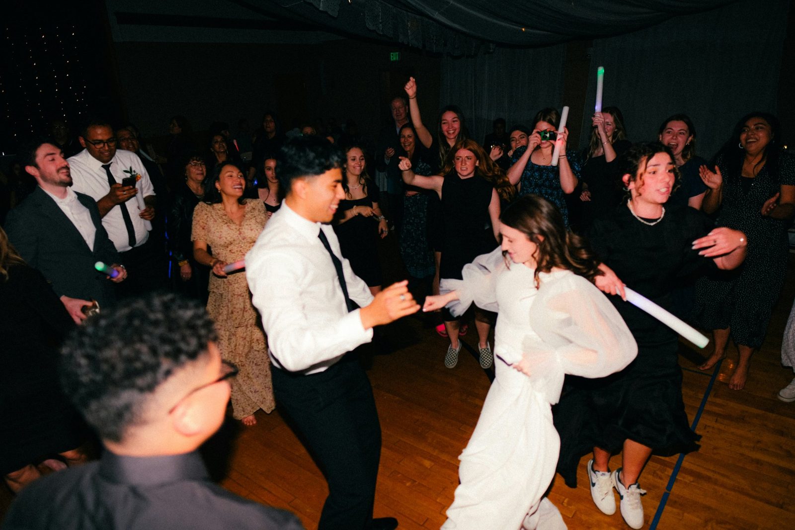 Guests dancing around the bride and groom, one taking a photo